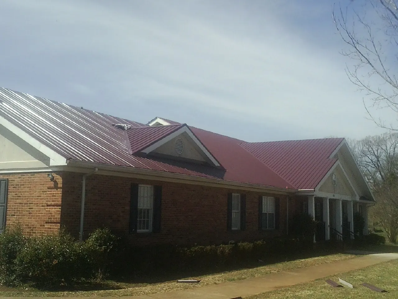 Red metal roof with gabled entries on a long brick building, from a Hail Damage Roof Repair job in Grafton