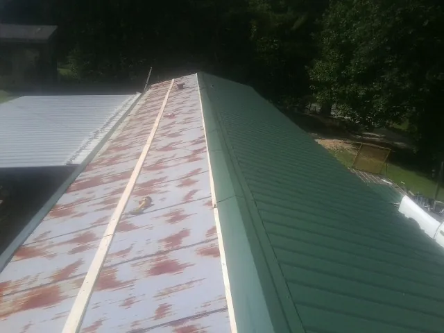 Old rusted panels beside newly installed green metal roofing — Wind Damage Roof Repair by Roofing Brothers in Grafton